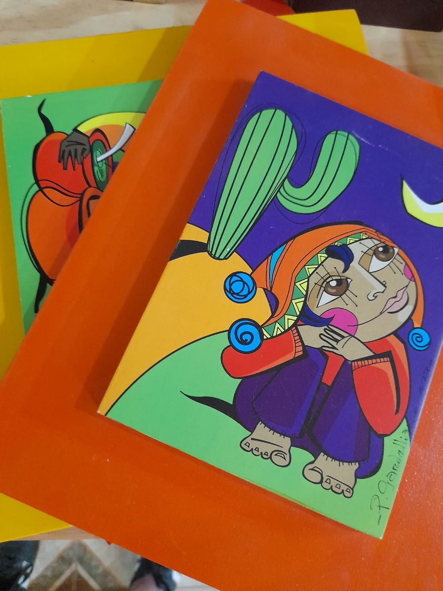 Cuadro pintado a mano con un cactus y una mujer de manto rojo, sobre fondo violeta y marco naranja
